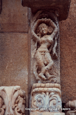 Weather worn sculpture of dancer on exterior temple wall.